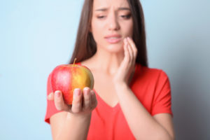Woman holding apple with pain in jaw